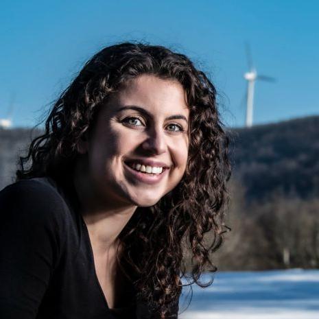 Andrea Poosikian在远处的三个风力涡轮机前微笑着.