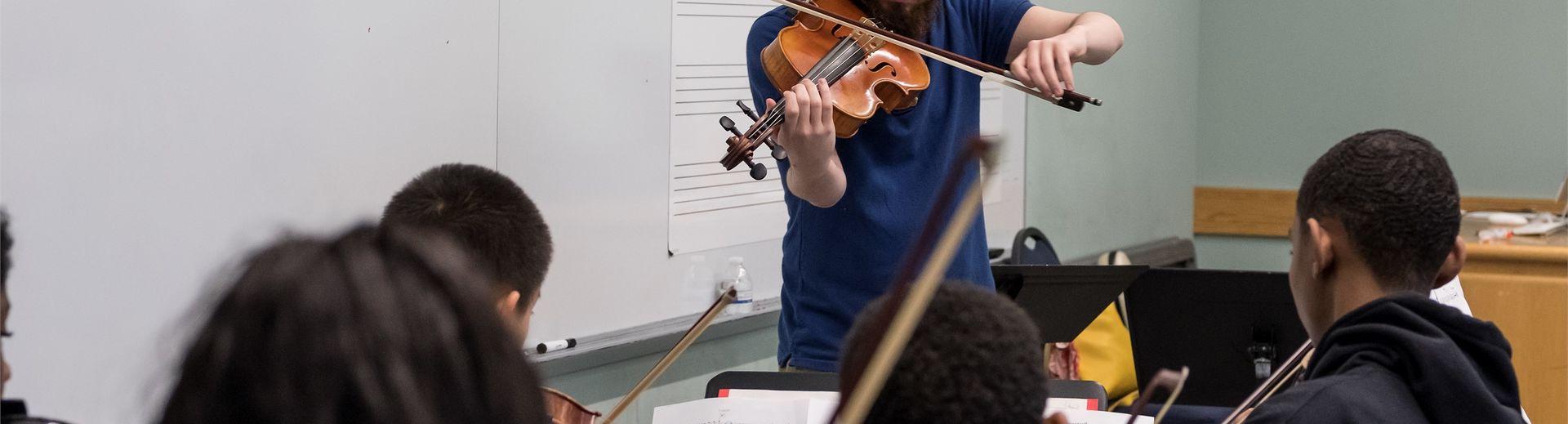 一位小提琴老师站在教室的前面，在年轻的学生面前演奏.