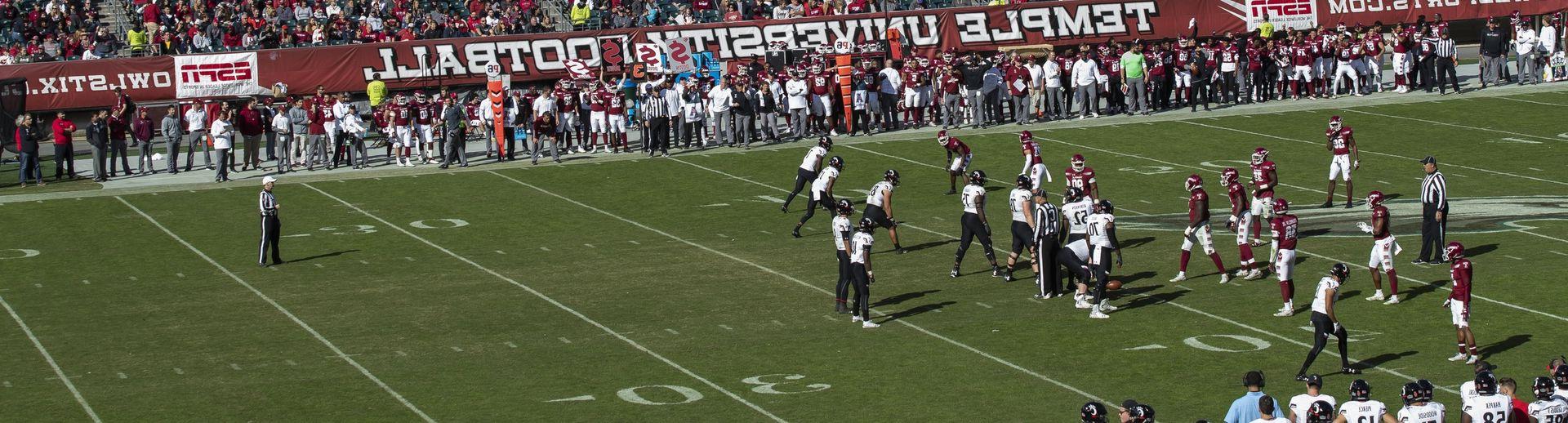 Temple University football players play a game while fans watch from the stands