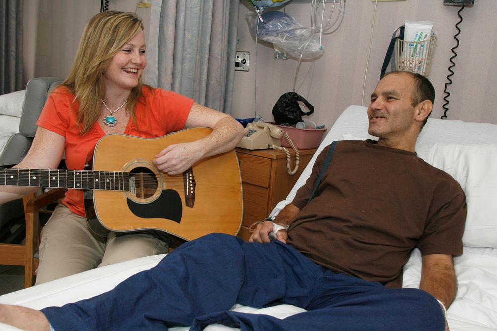  A music therapist plays guitar for a hospital patient.