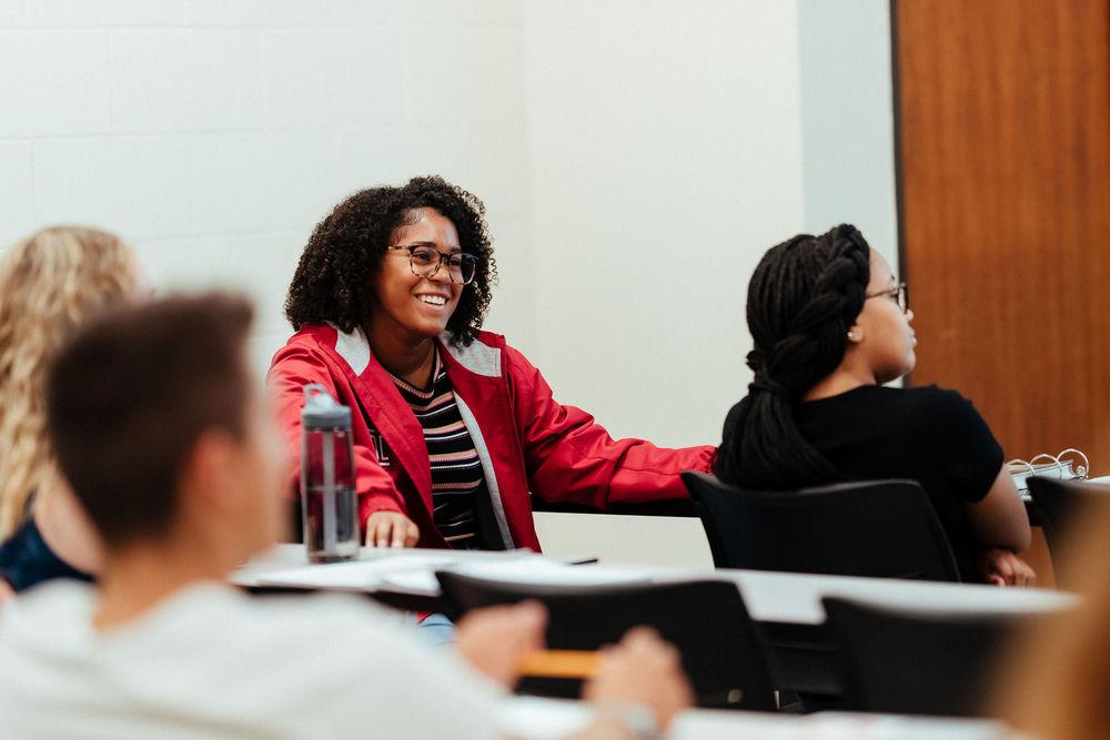 一位穿红色夹克的女学生在课堂讨论中微笑.