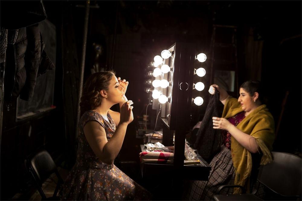 Two female students apply makeup backstage before a show.