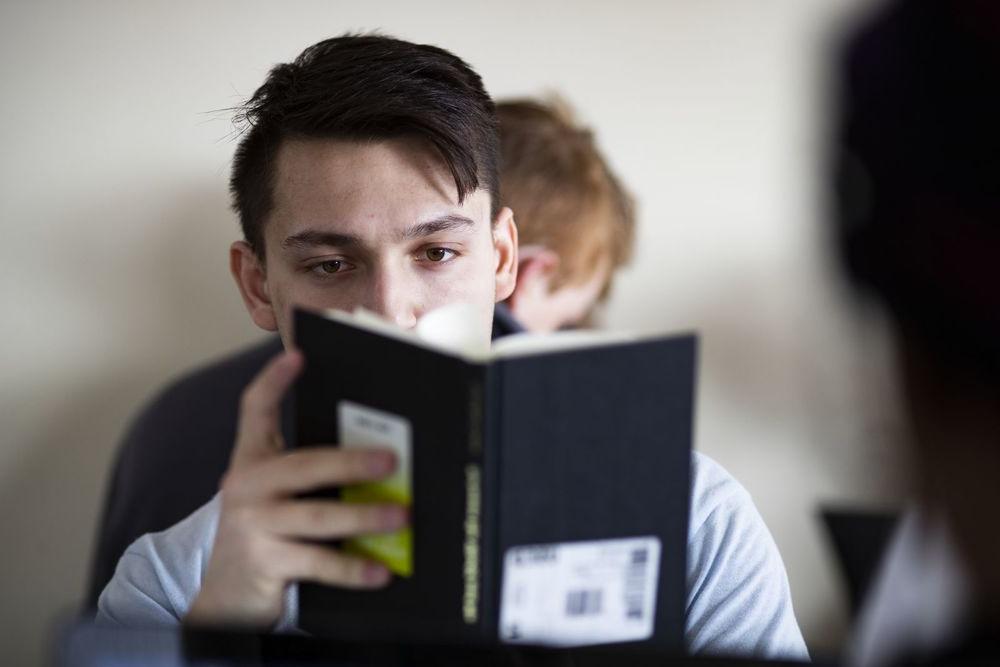 一个男学生的脸被他正在读的书遮住了.