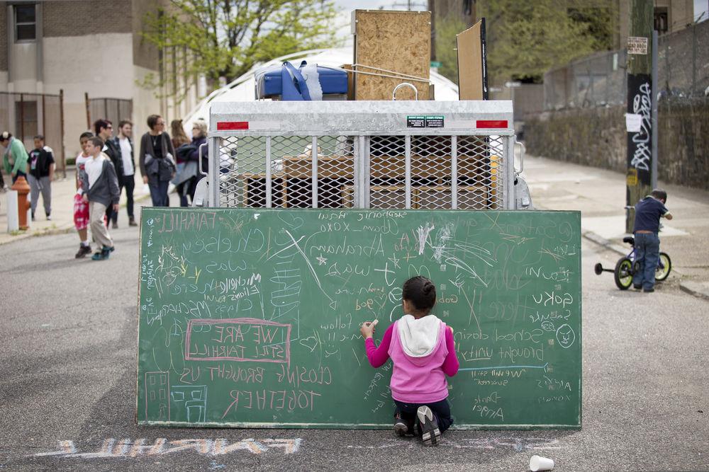 An image of a child writing on a chalkboard in a busy street