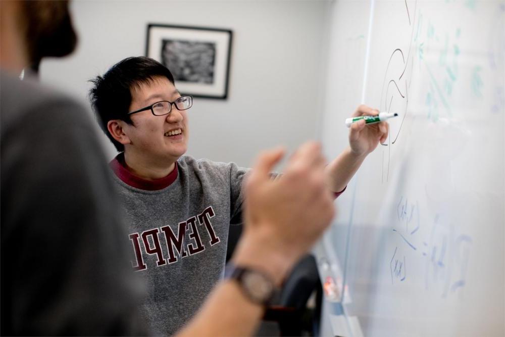 天普教室里，学生在白板上写数学方程式，科技学院教授在一旁看着. 