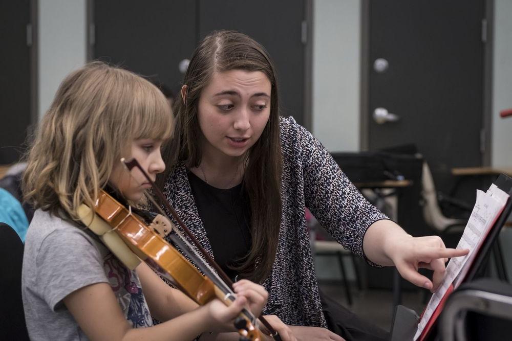 A Temple music student works with an elementary school student during a violin lesson.